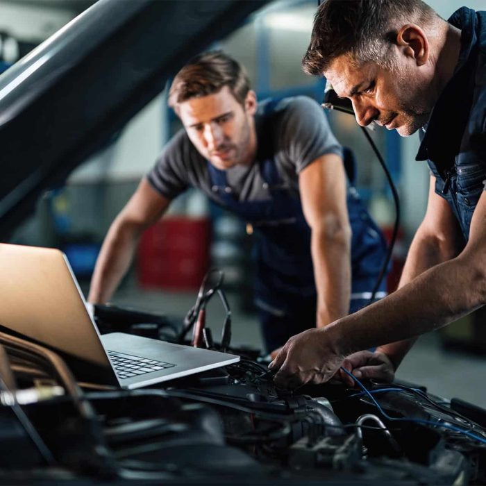 Car repairmen using laptop while doing car engine diagnostic in auto repair shop.